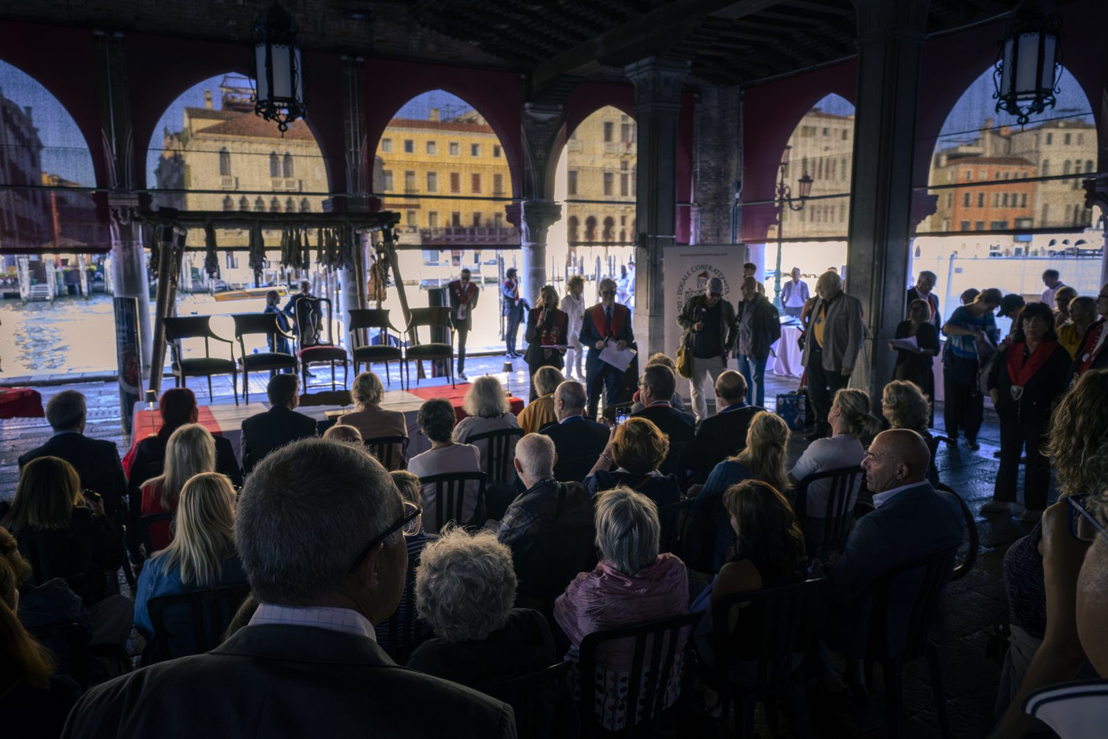 Il pubblico seduto nella loggia del Mercato del Pesce di Rialto, con gli archi aperti sul Canal Grande