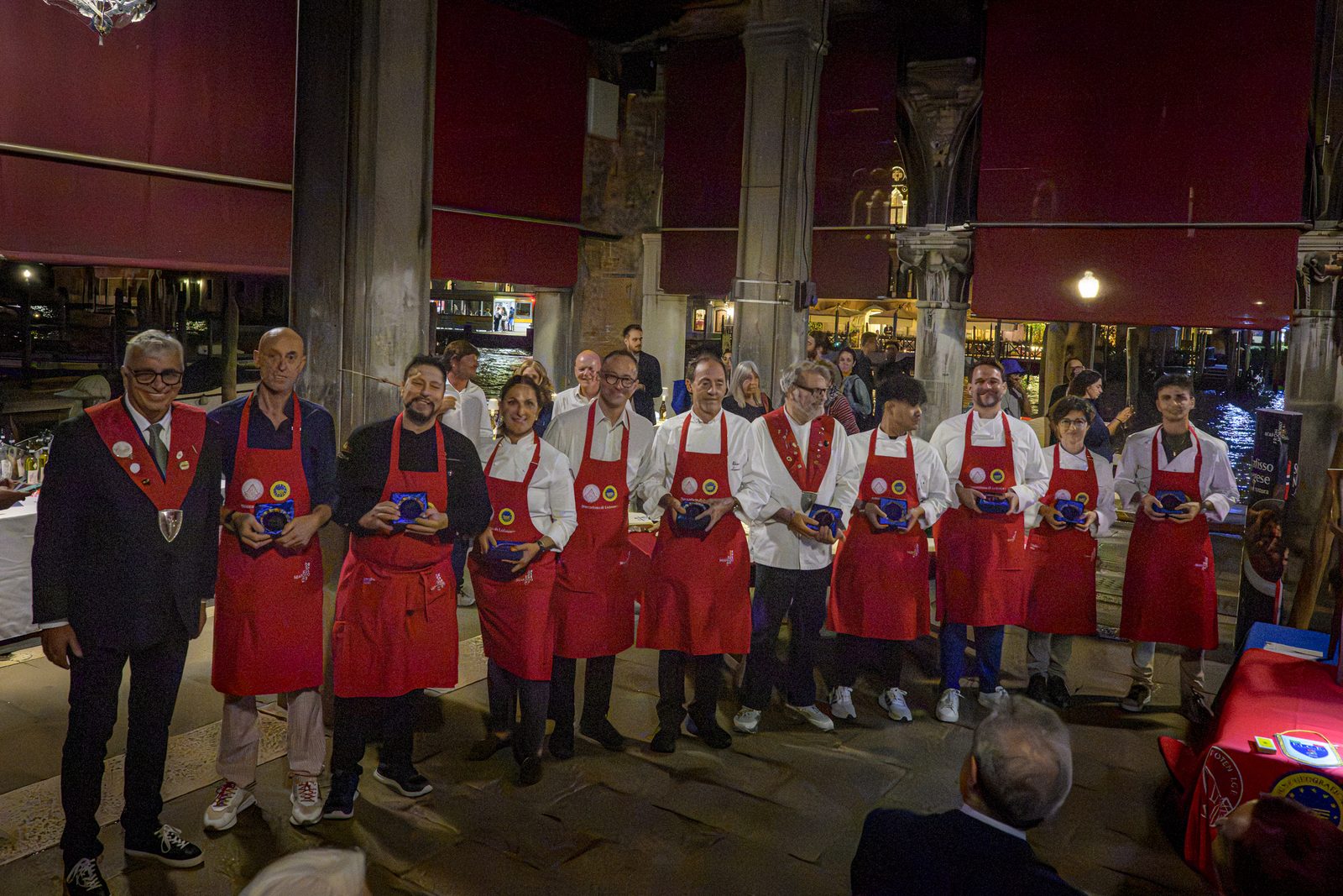 I ristoratori della Rotta in grembiule rosso, in fila nella loggia, ciascuno con il riconoscimento della Dogale